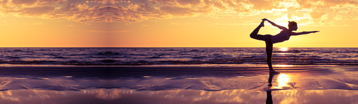 Woman doing a yoga pose in front of a beach sunset